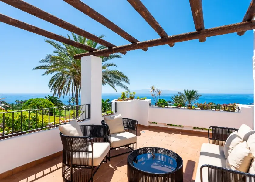 Luxury terrace with woven lounge chairs, rustic wooden pergola, ocean vista, Mediterranean architectural style