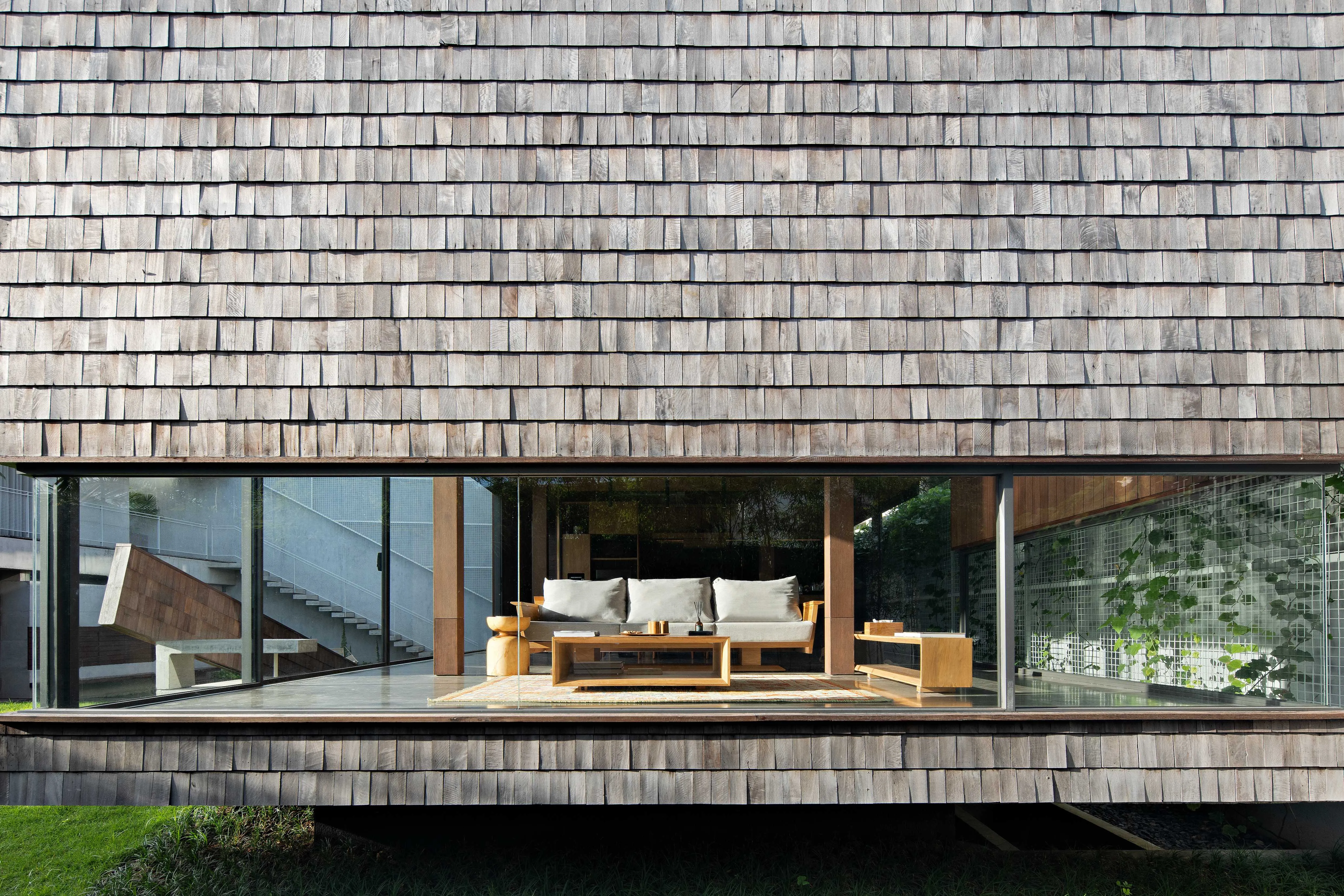 Contemporary Villa Tana Takah with weathered cedar shake exterior, expansive floor-to-ceiling windows, minimalist wooden furniture, clean lines reminiscent of alpine architecture, and serene natural surroundings