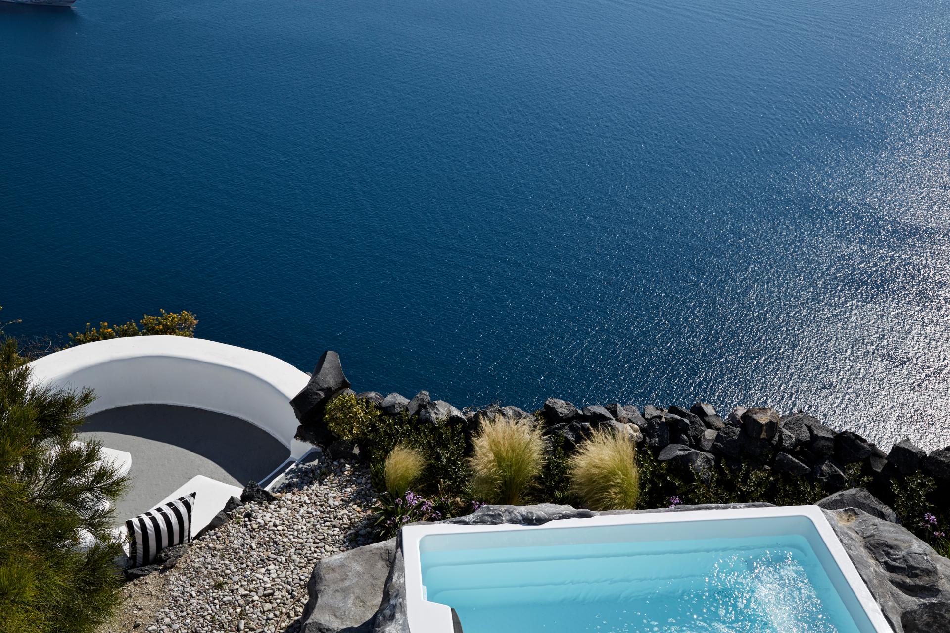 Minimalist coastal villa with white curved architecture, turquoise plunge pool, and rocky Mediterranean shoreline