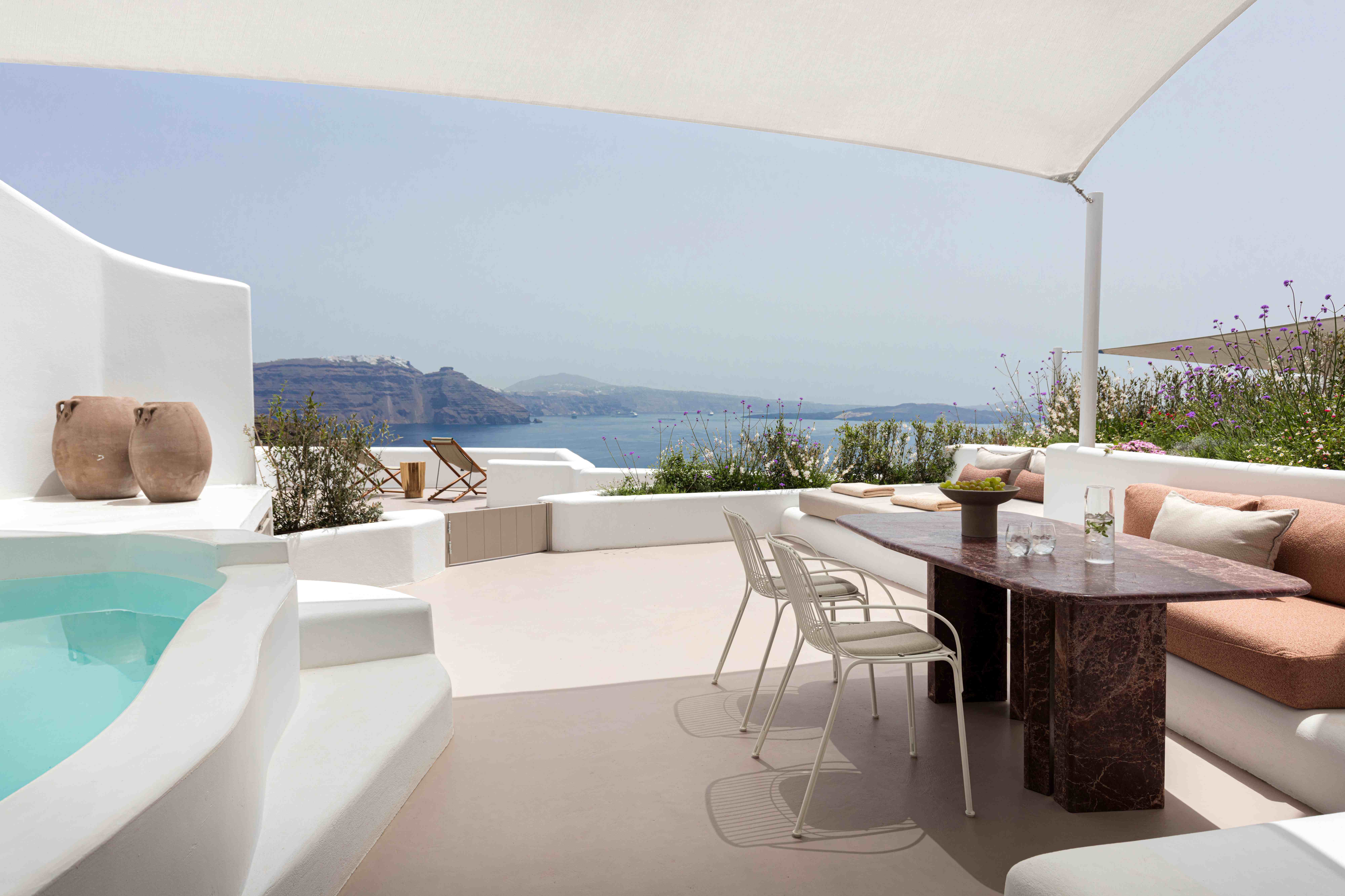 Modern white villa terrace with heated plunge pool, dining area, and panoramic sea views overlooking the caldera