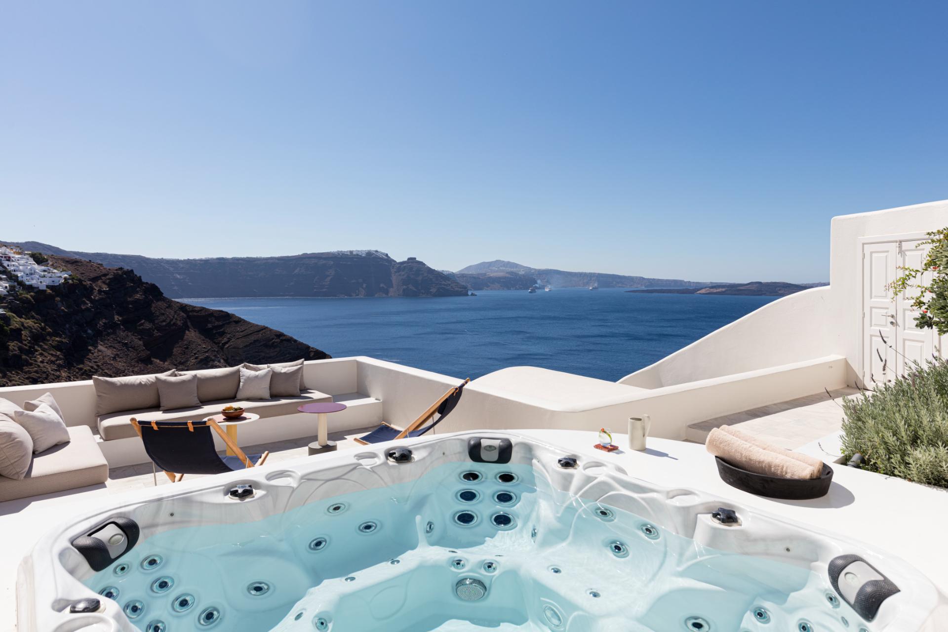 Luxury hot tub overlooking Santorini caldera with white seating and dramatic Aegean Sea views