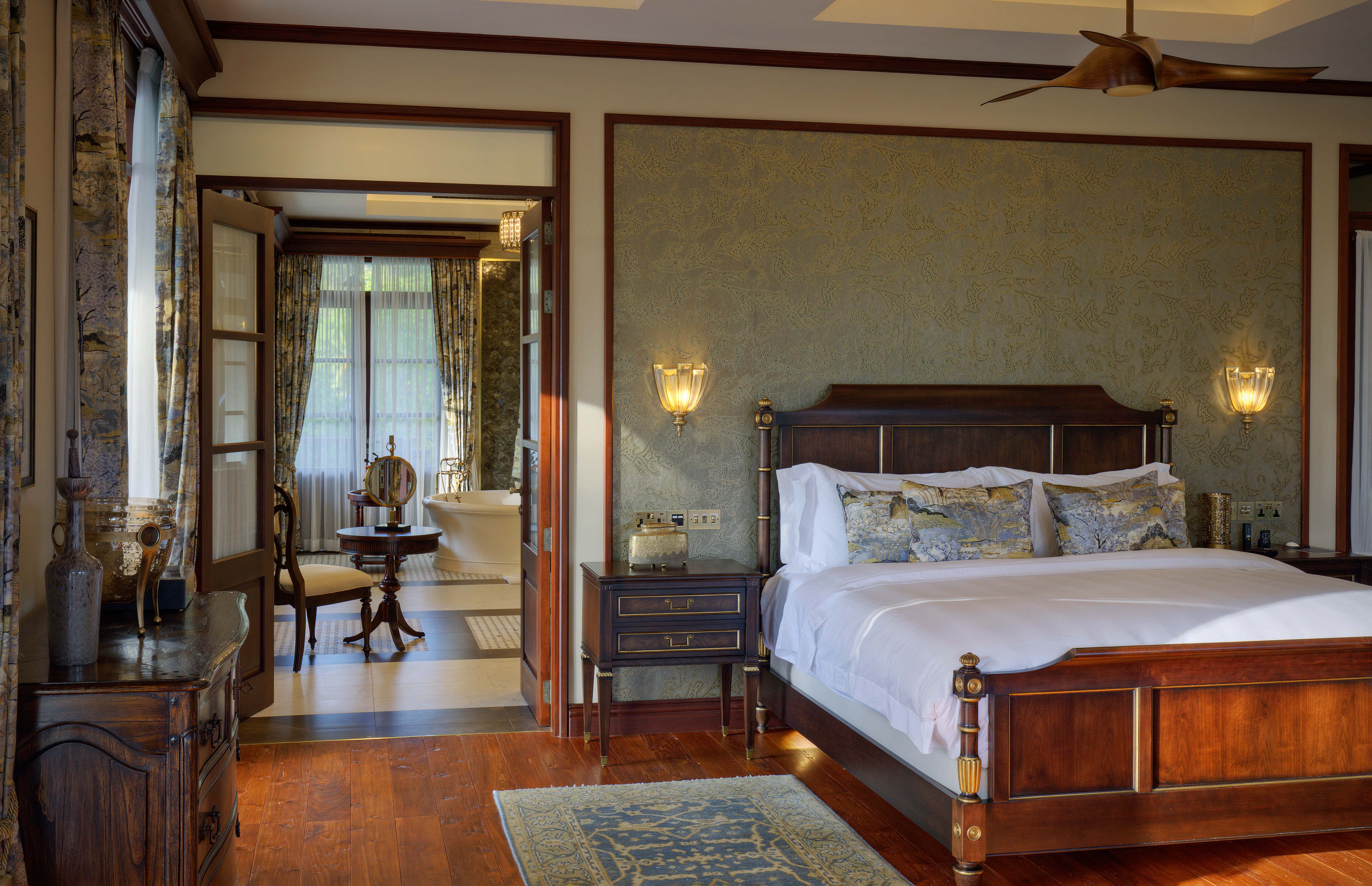 Luxurious bedroom suite with dark wood four-poster bed, damask wallpaper, and elegant furnishings
