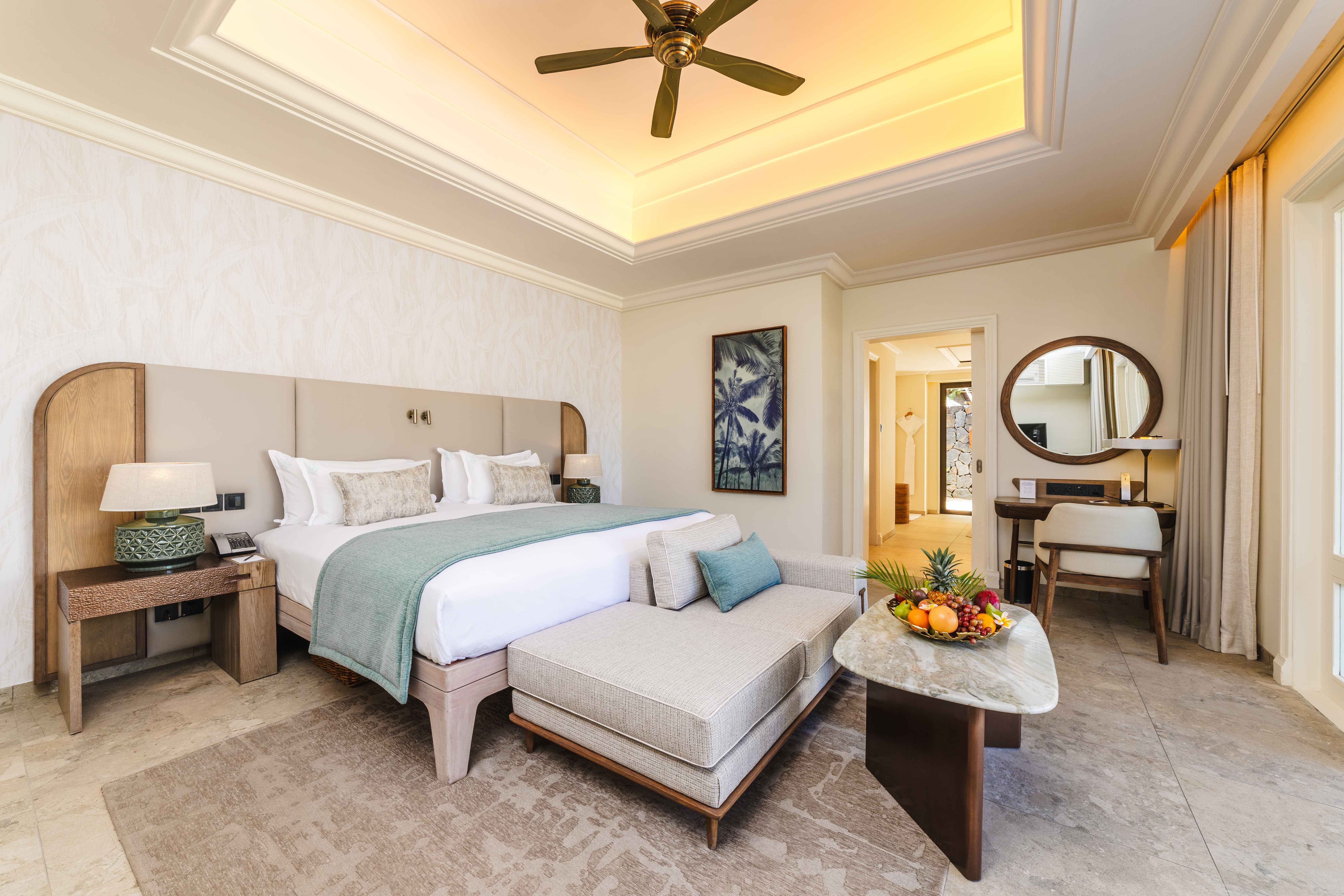 Luxurious hotel bedroom suite with marble furnishings, warm wood tones, modern ceiling fan, and elegant decor