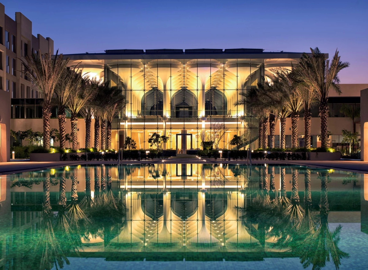 Kempinski Hotel Muscat illuminated at night with modern glass architecture, palm trees, and reflecting pool